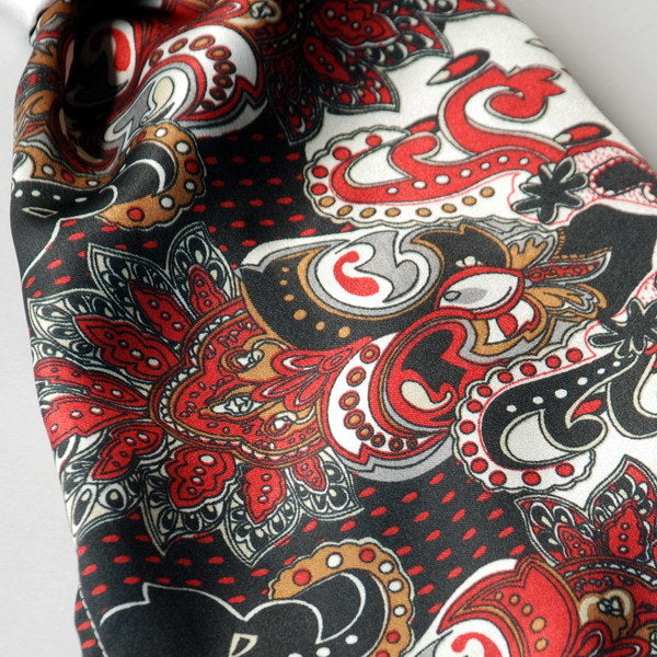 Close-up paisley scarf fabric in black, red, gray, and white with ornate motifs.