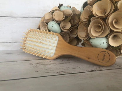 Wooden detangling hair brush with white pin bristles on light wood base