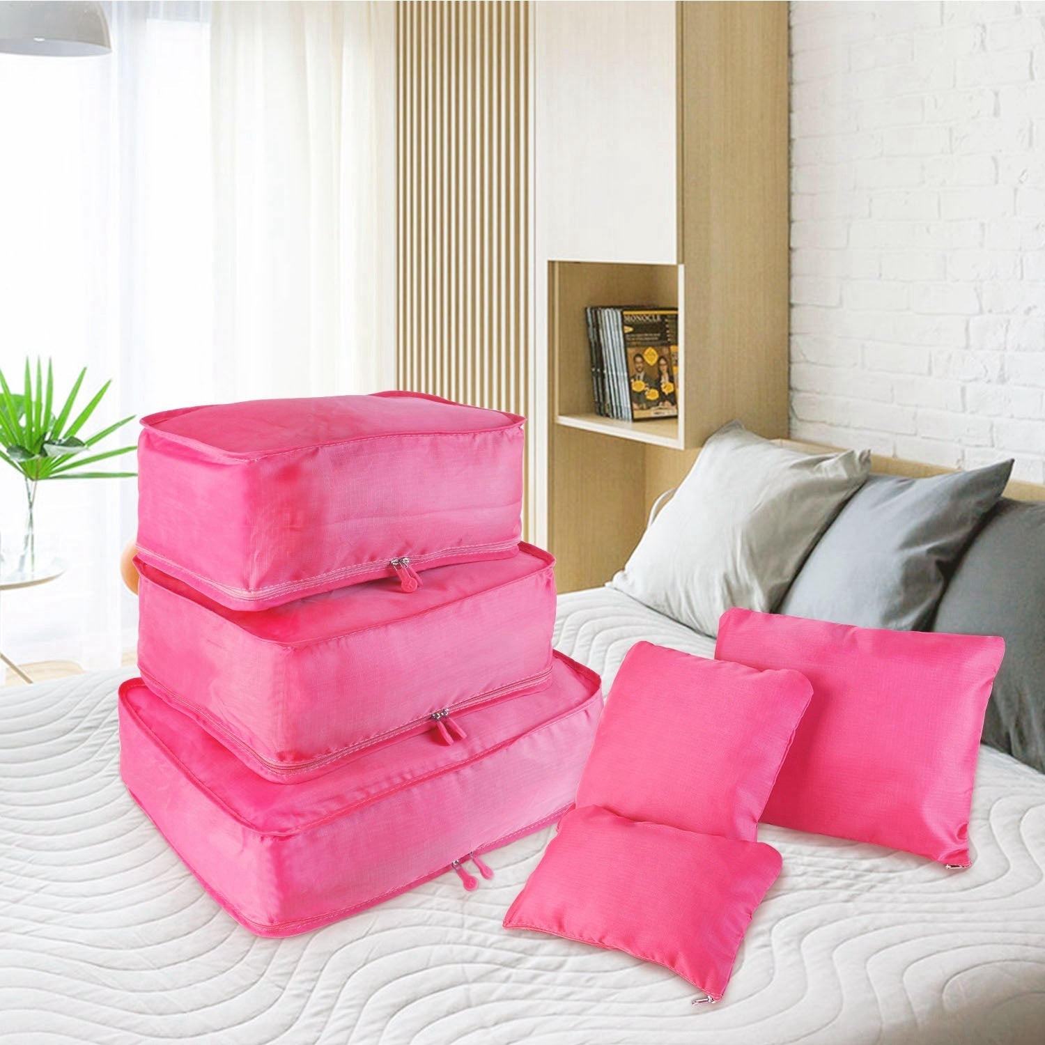 Pink travel clothing organizer cubes and foldable pouches on a bed