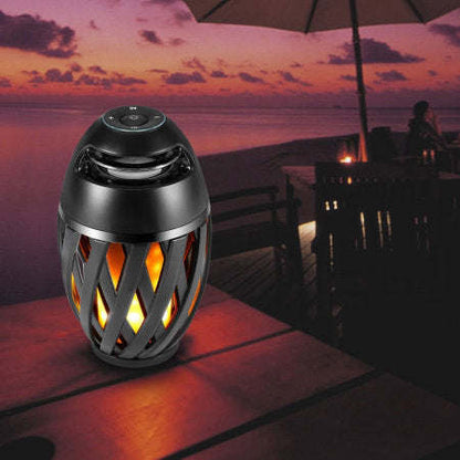 Outdoor LED torch speaker, black lantern top with glowing amber flame-pattern, close-up view.