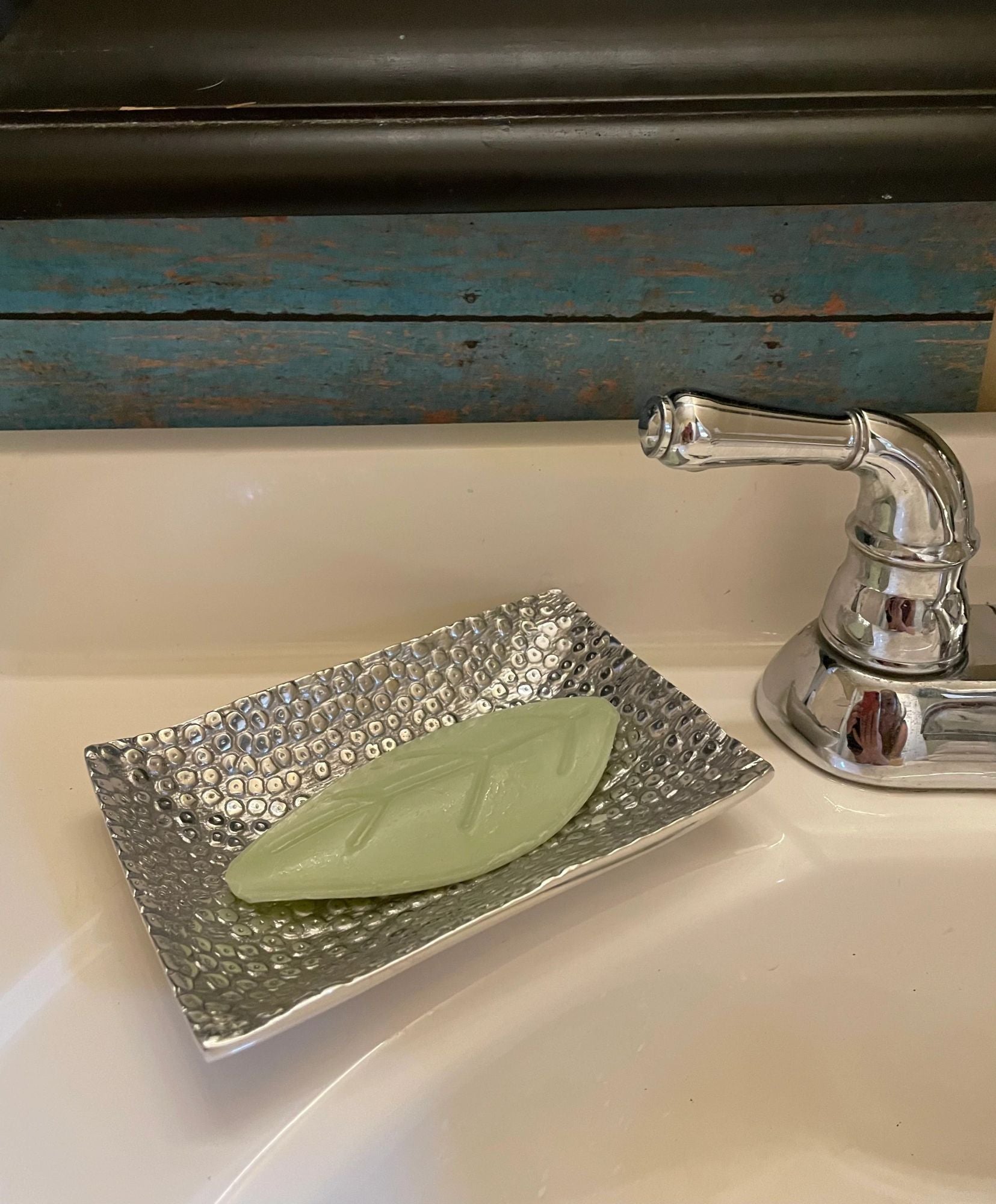 Rectangular hammered metal dish holding a pale green soap bar near the faucet