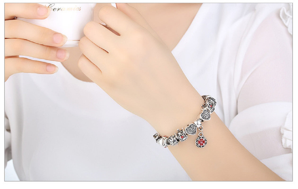 Silver charm bracelet on wrist with red enamel flower pendant and heart charms