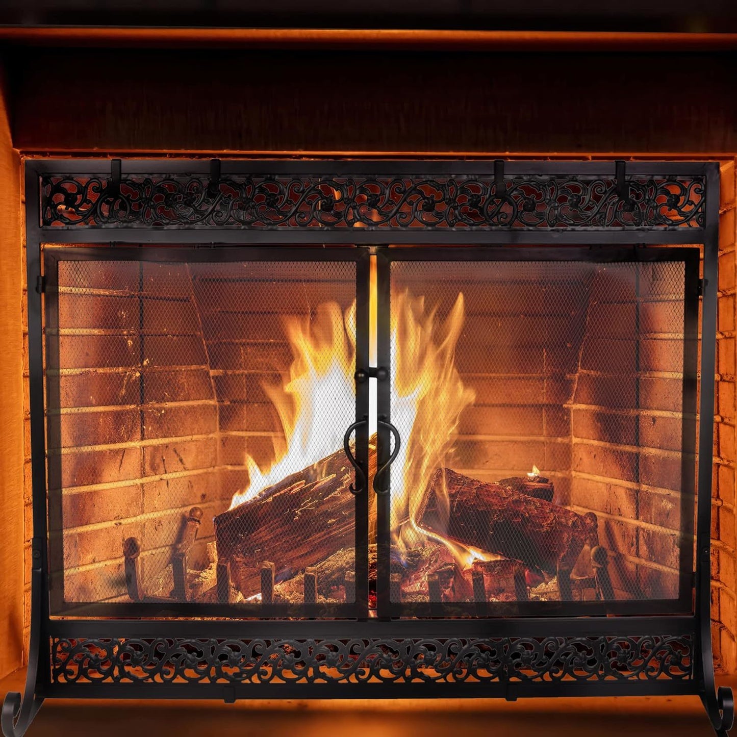 Black metal fireplace screen with two mesh doors in front of burning logs