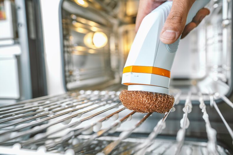 Cordless scrub brush with brown round brush head scrubbing a metal rack