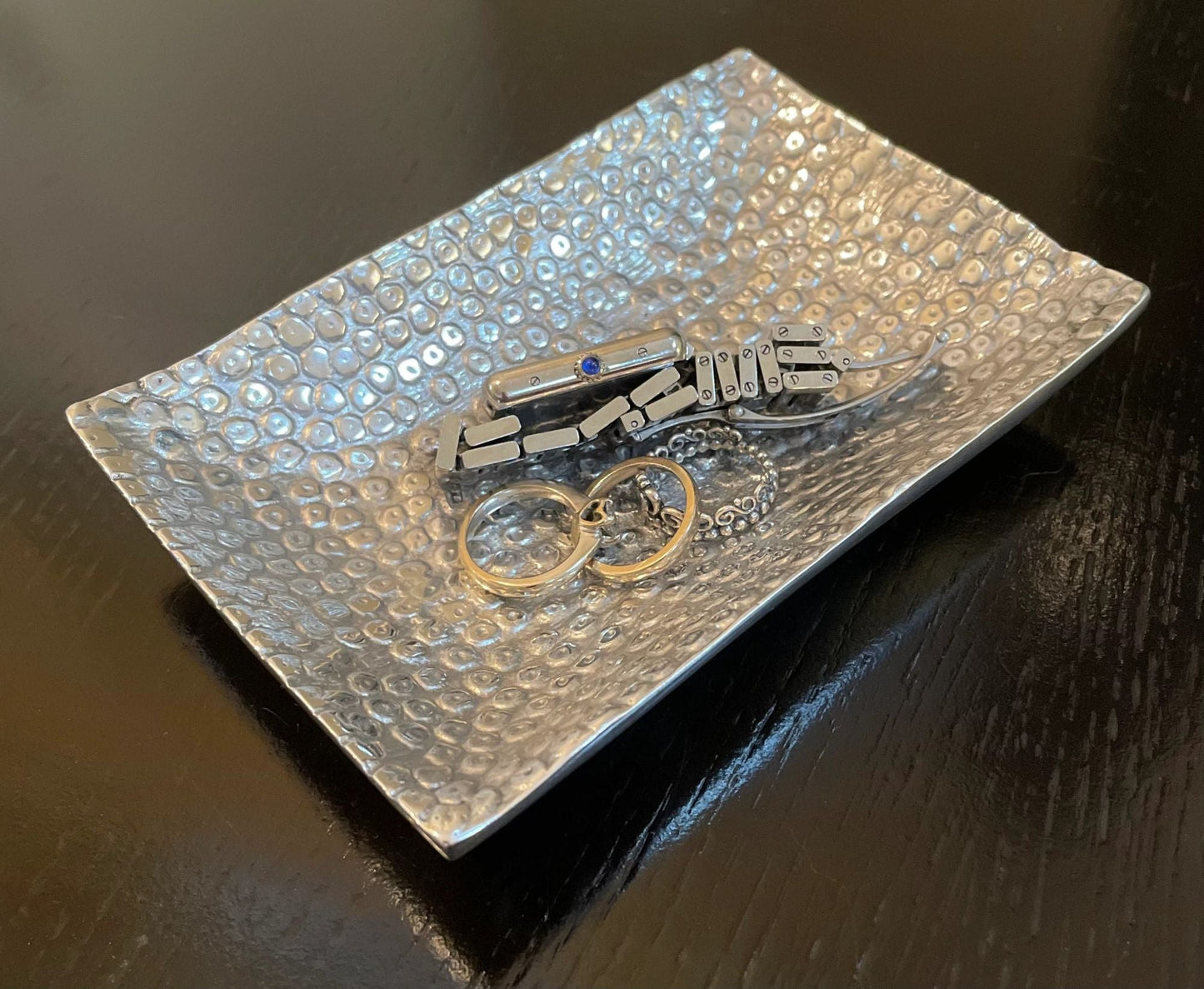 Rectangular hammered metal tray holding a metal ring and clasp jewelry piece