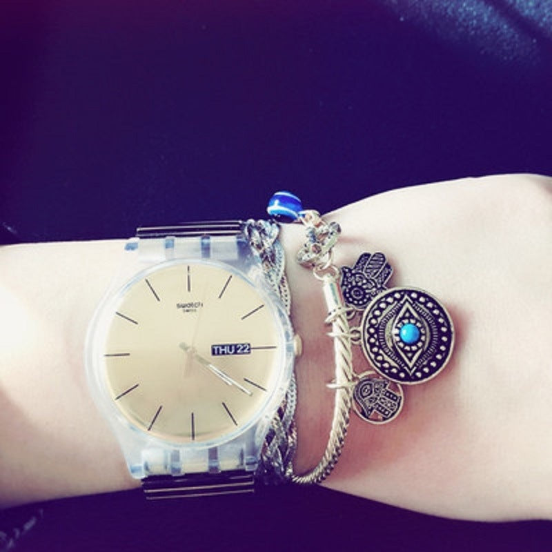 Silver-tone twisted charm bracelet on wrist with evil eye and hamsa charms, blue enamel details.