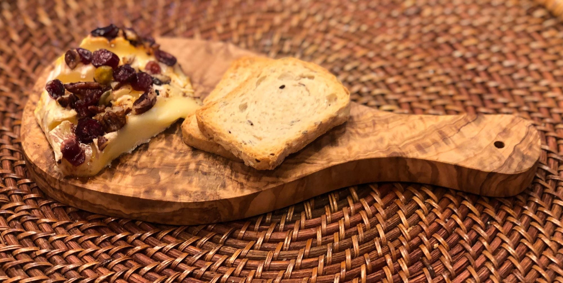 Olive-wood cutting board with handle, bread slices and cheese topping
