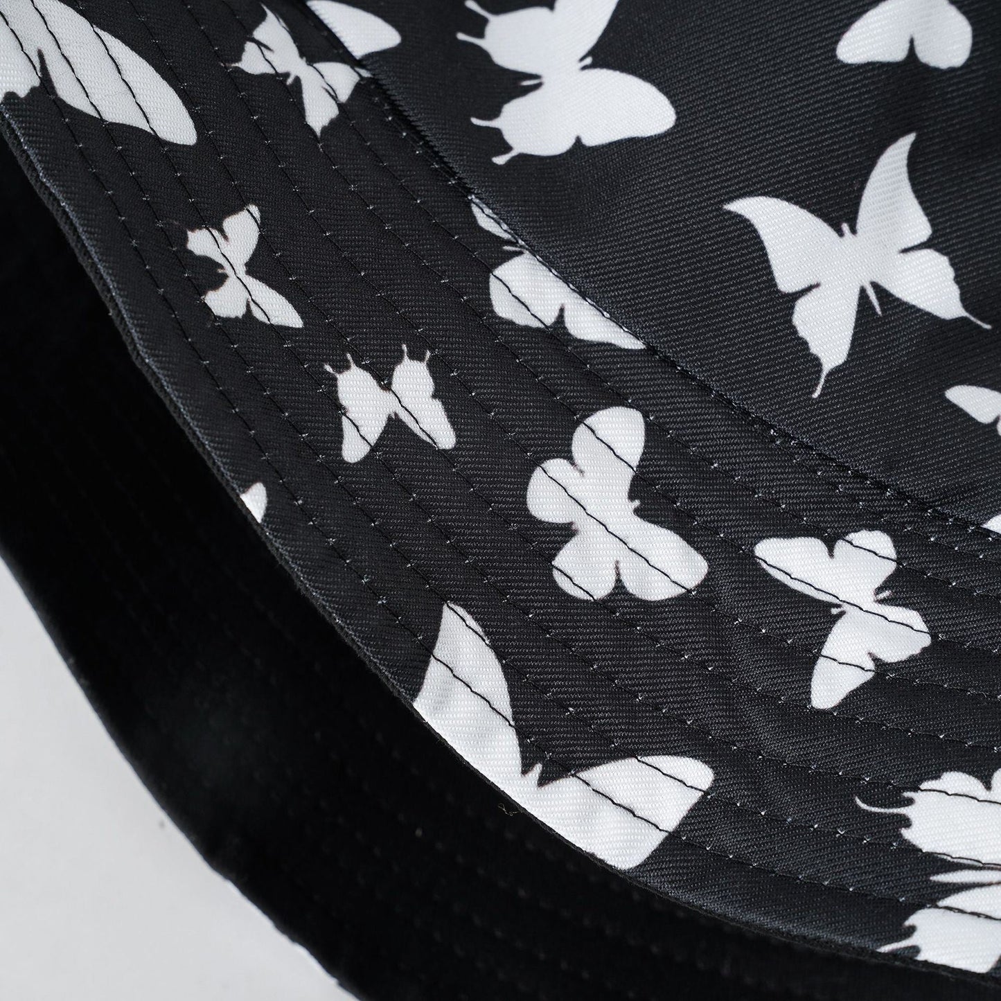 Black bucket hat fabric with white butterfly silhouettes, stitched texture