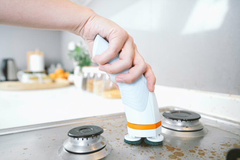 Cordless power scrub brush cleaning stovetop burners in a kitchen