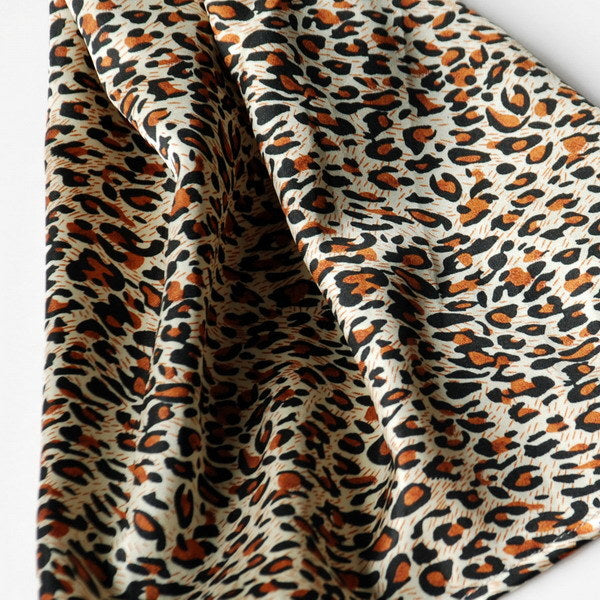 Leopard-print silky scarf fabric close-up with cream, brown, and orange tones