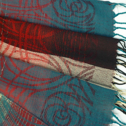 Pashmina scarf close-up, teal and red woven bands with beige section and fringes.