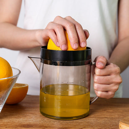 Manual citrus juicer: hand presses citrus into black squeezer top over clear pitcher