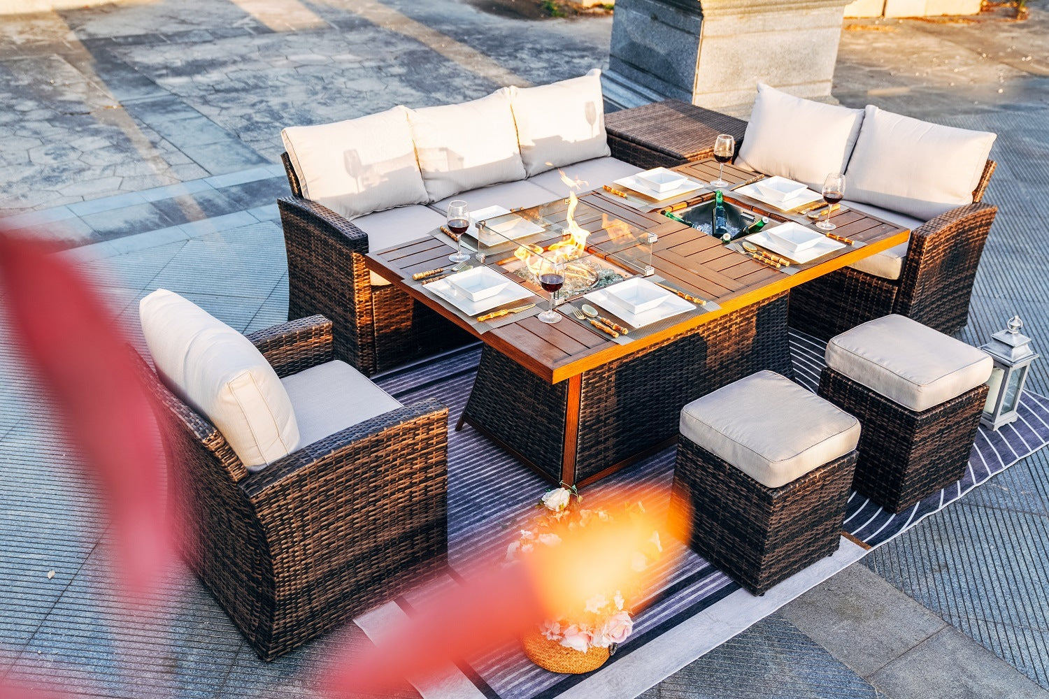 Patio conversation sofa set with glass-topped table, cushioned ottomans, and flaming firepit