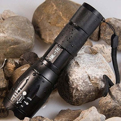 Black zoomable focusing flashlight with textured grip and lanyard, on rocks