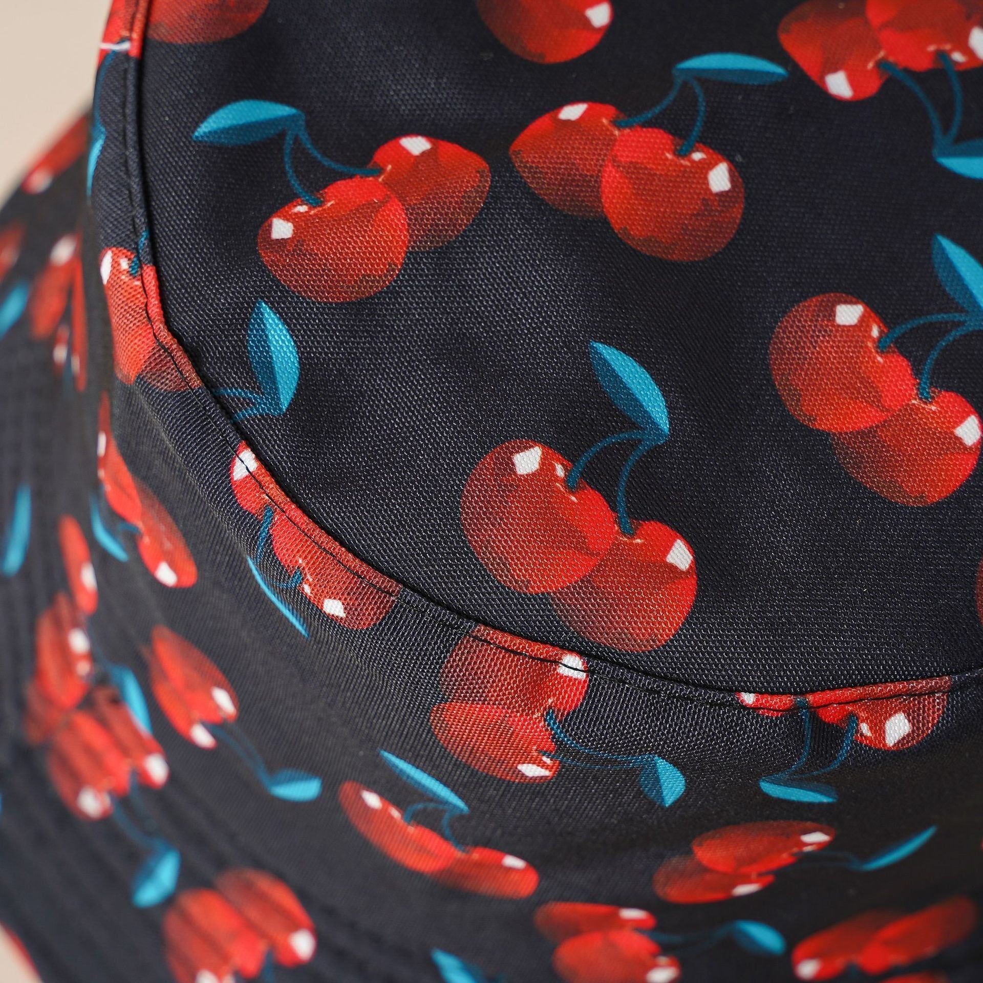 Double-sided cherry bucket hat close-up, dark brim with red cherries and blue leaves