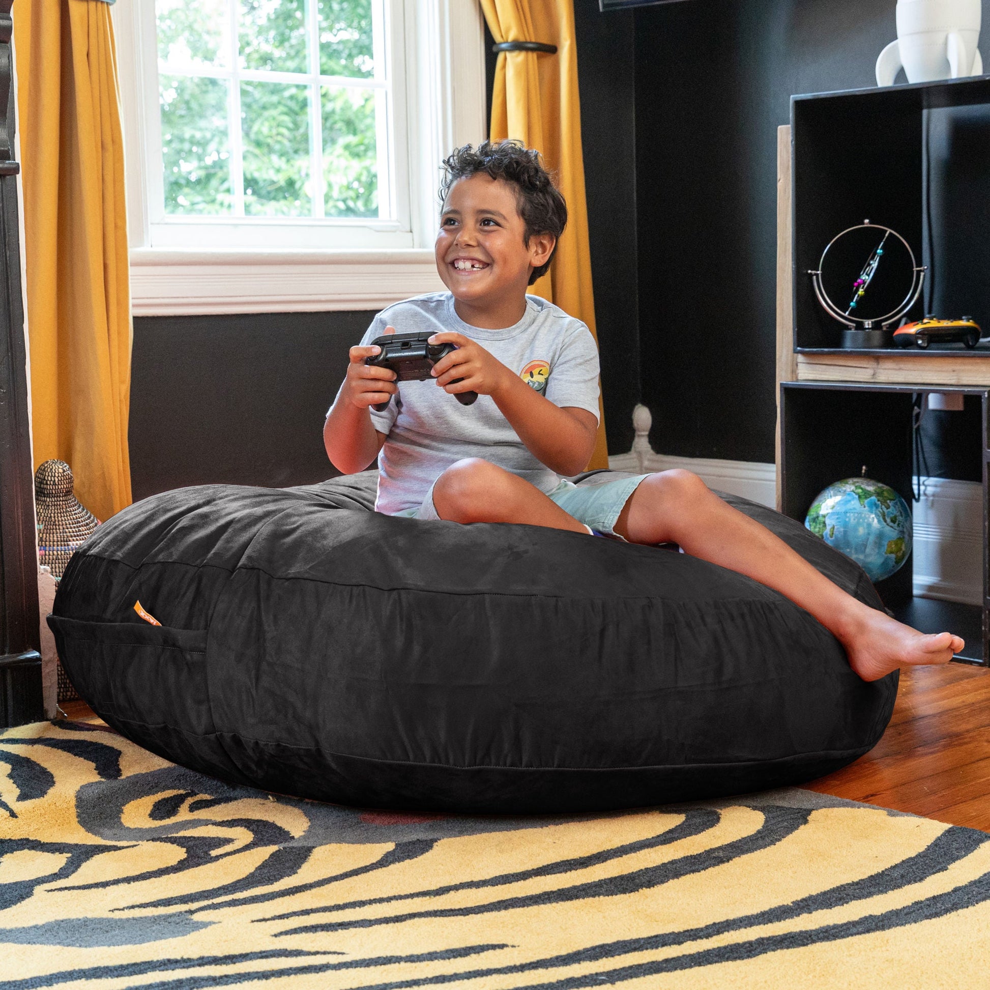 Black kids cocoon bean bag with microsuede cover, child lounging on top.