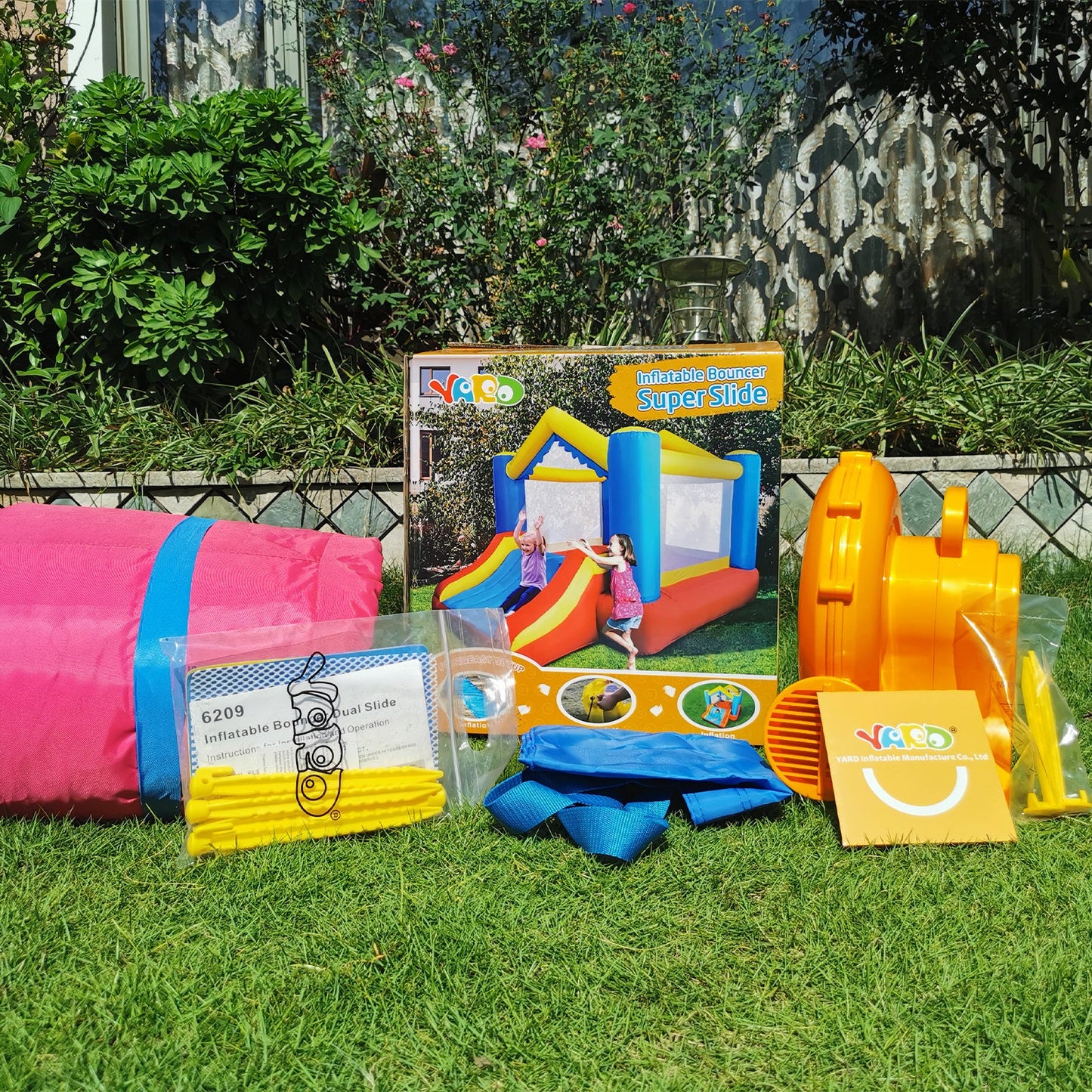 Inflatable bounce house set with accessories in yard; red, blue, and yellow inflatables