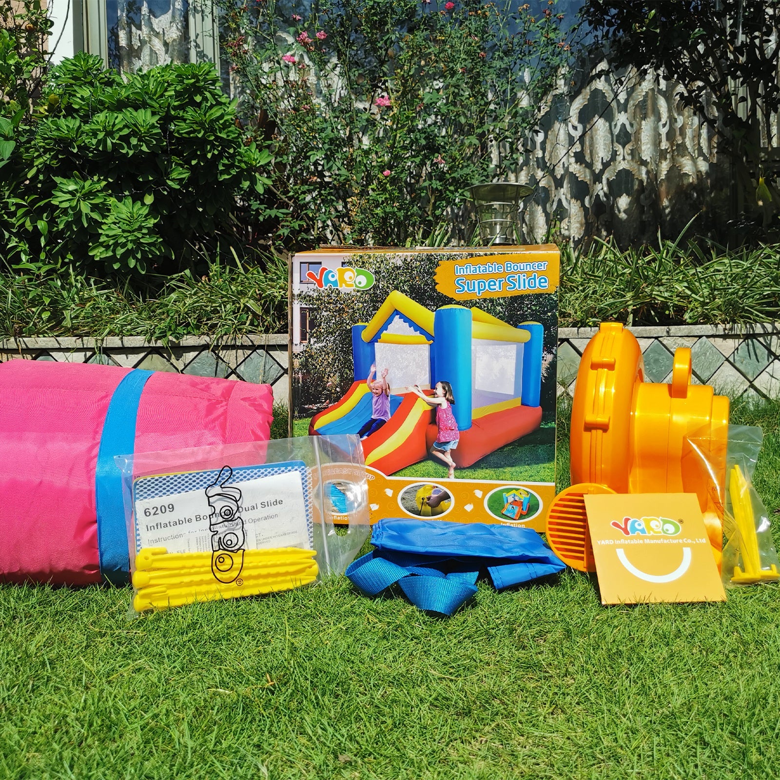 Inflatable bounce house set with accessories in yard; red, blue, and yellow inflatables
