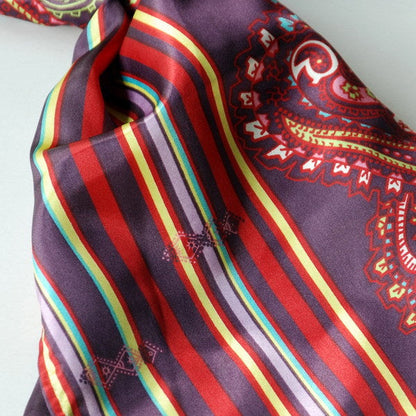 Silk scarf close-up with multicolor rainbow stripes and red paisley motifs on dark purple