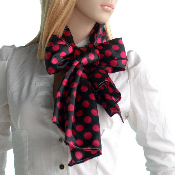 Silk scarf with red polka dots on black, tied in a bow at the neck.