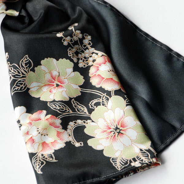 Black silk scarf close-up with beige, pink, and green flower pattern and gold vines