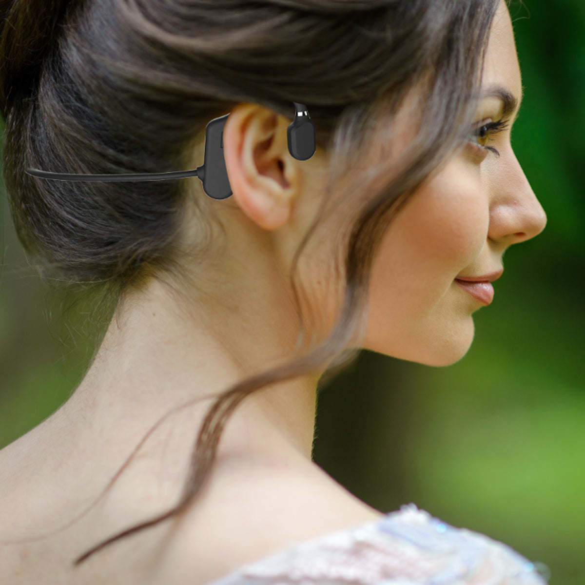 Open-ear wireless headphones worn behind the ear, shown in side profile on a woman.