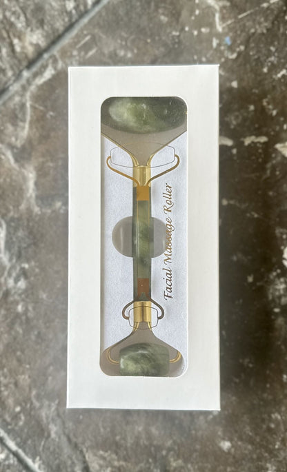Jade facial roller in retail box with clear window, showing green stones and gold frame