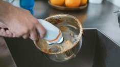 Hand using scrub attachment with orange-and-gray head over a bowl of water