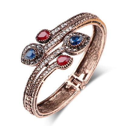 Rose-gold tone bypass bangle with red and blue oval stones and clear CZ sparkle