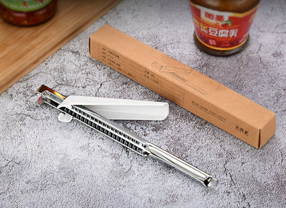 Stainless steel jar lid opener with white handle and serrated grip beside cardboard boxes.
