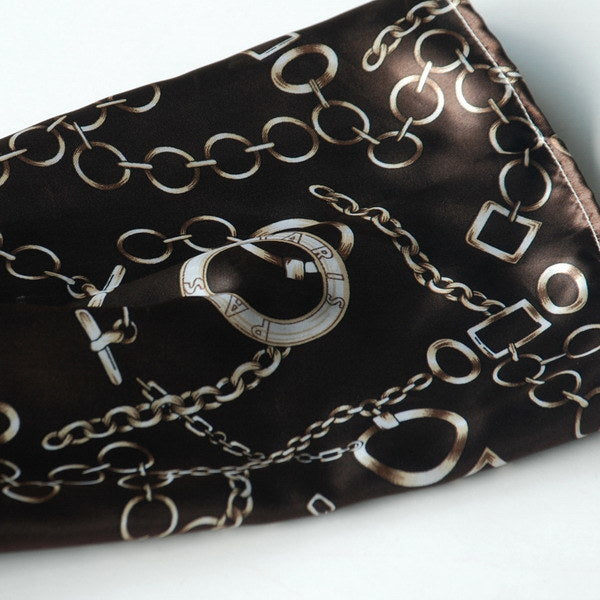 Large silk scarf close-up, dark fabric with gold chain and lock motifs.