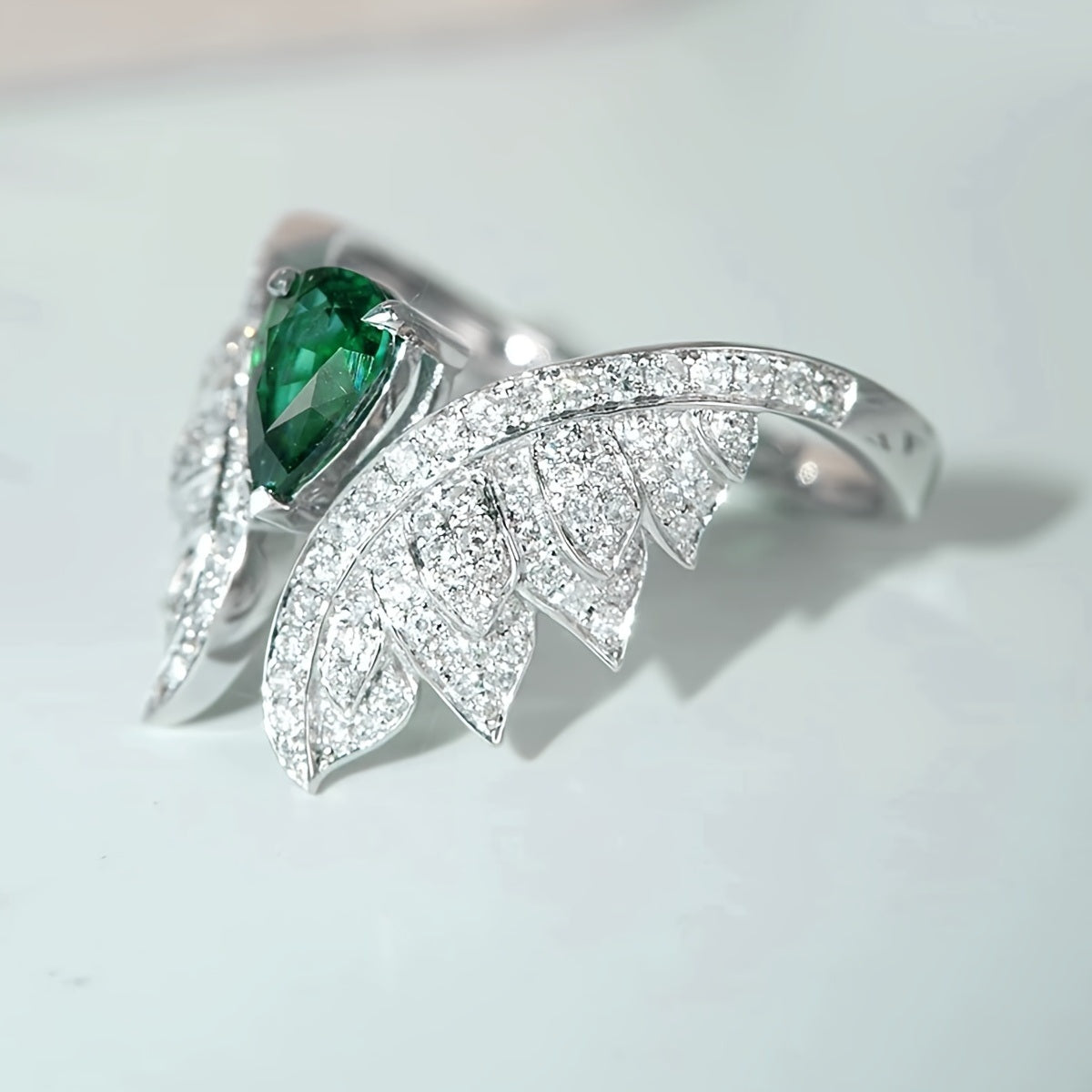 Angled view of silver-tone zircon wing ring with green pear center stone