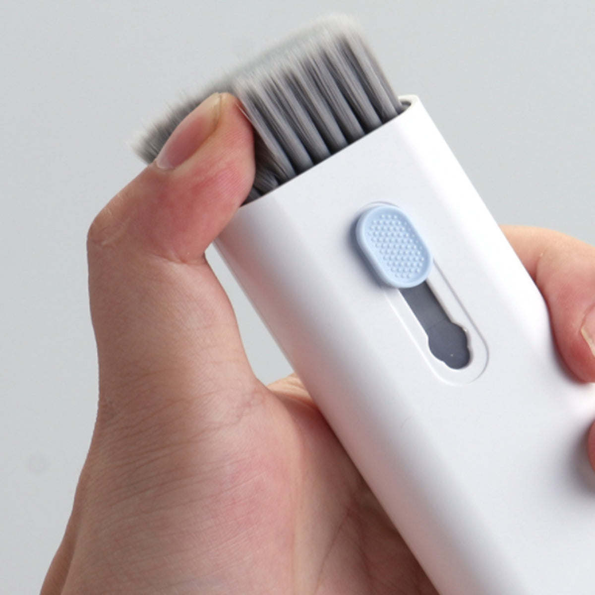White handheld cleaning gadget with gray bristle brush head and oval control pad