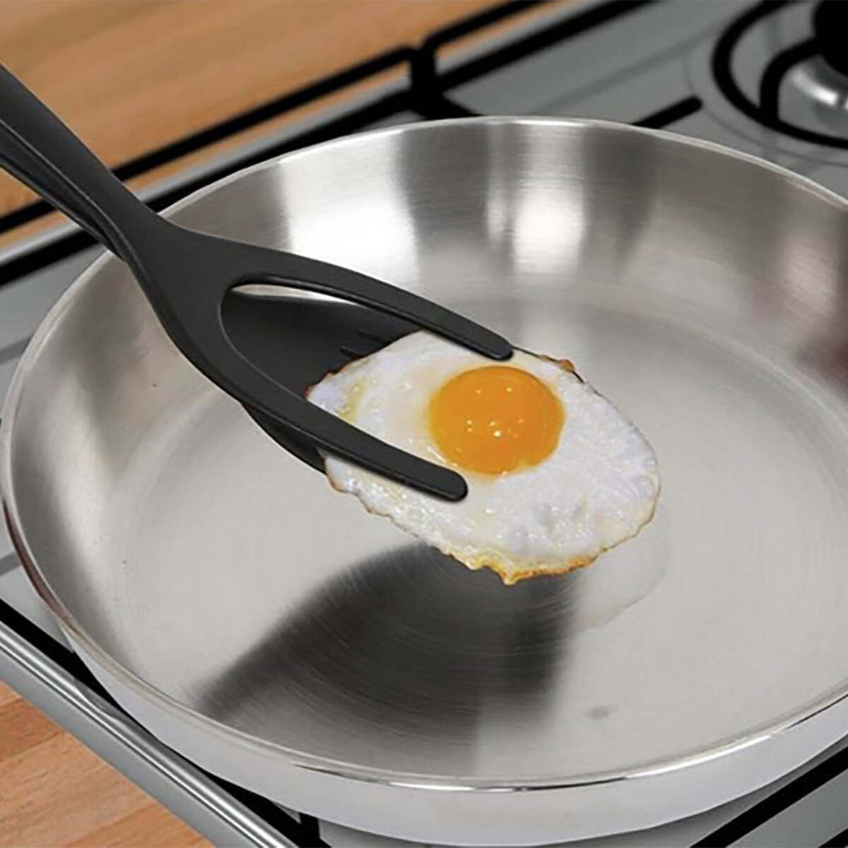 Frying pan with black egg-shaping spatulas holding a sunny-side egg.