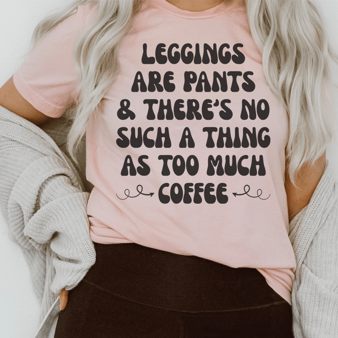 Pink crewneck T-shirt with black slogan graphic: 'Leggings are pants & too much coffee'