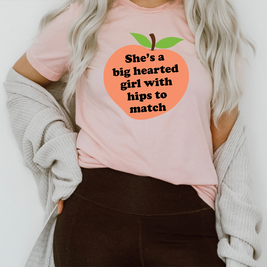 Pink graphic t-shirt with orange heart logo, green leaves, and “hips to match” text.