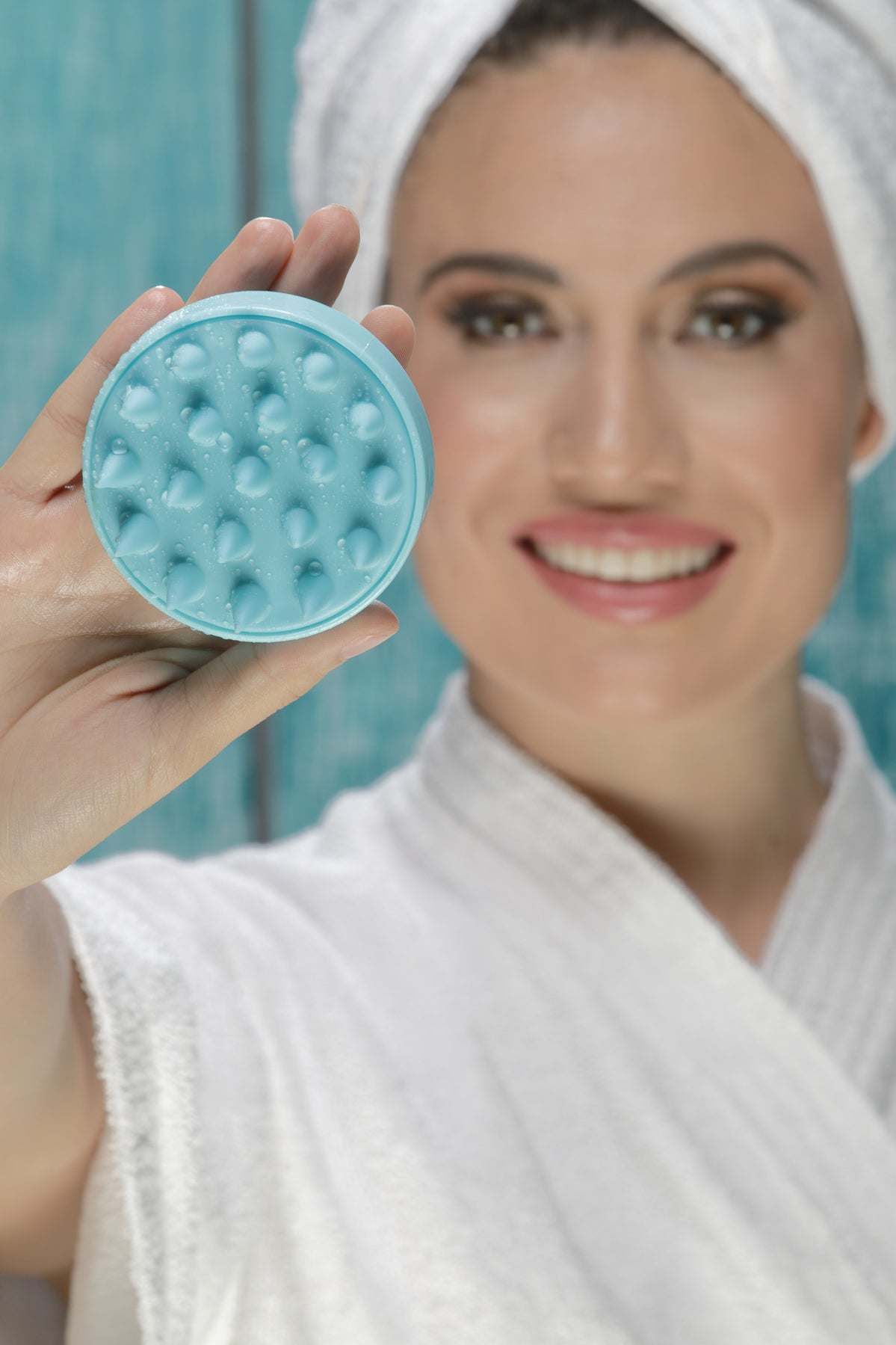 Aqua silicone scalp massager brush held near face, round head with soft spikes