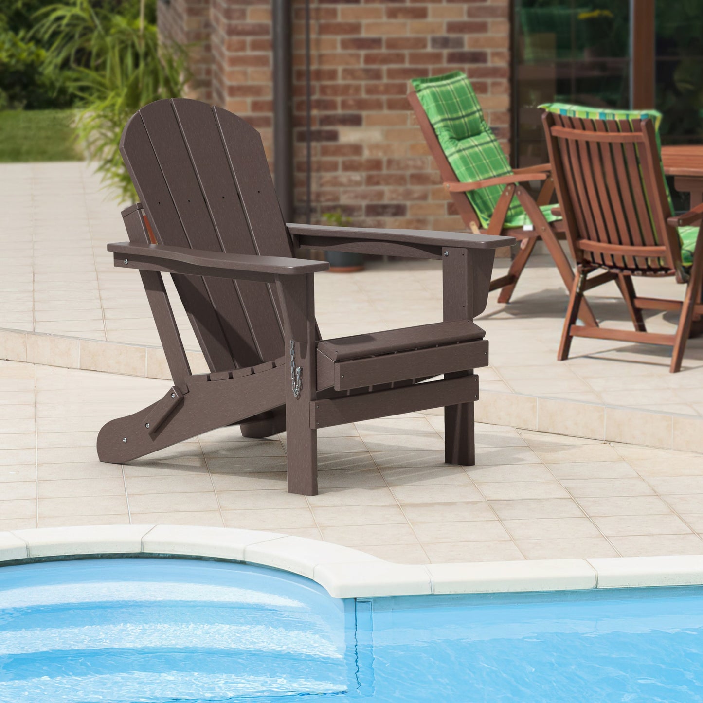 Folding adirondack chair in dark brown beside a pool on a patio