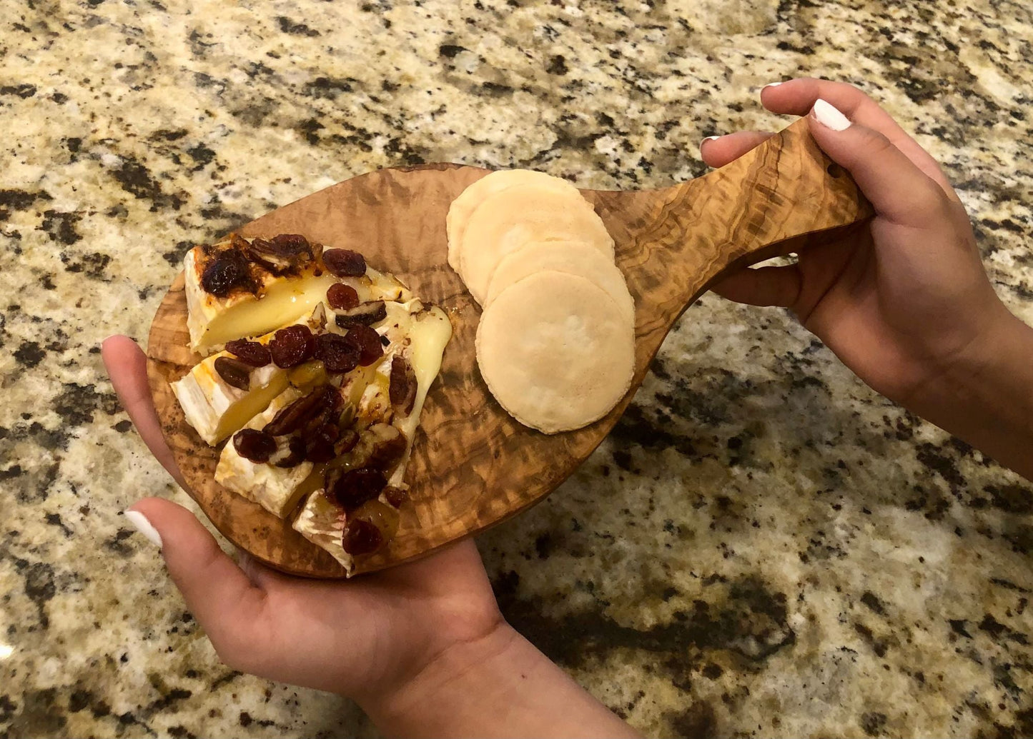 Wood cutting board with oval handle holding bread and sliced cheese