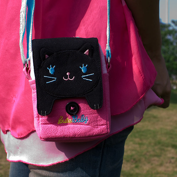 Embroidered cat swingpack bag in pink with black front pocket and light blue strap.
