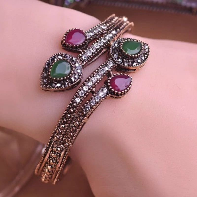 Rose-gold tone bypass bangle on wrist with green and purple oval stones and clear CZ halos