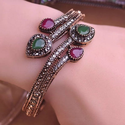 Rose-gold tone bypass bangle on wrist with green and purple oval stones and clear CZ halos