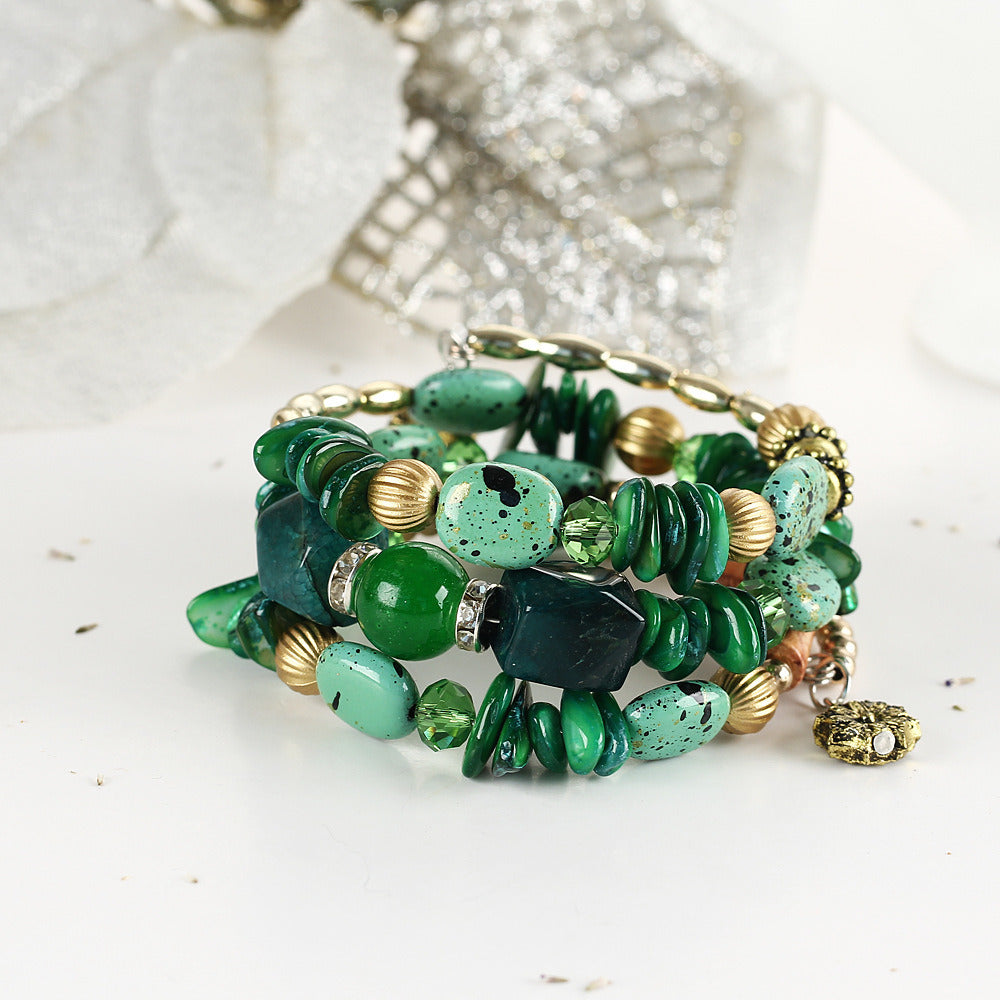 Green boho charm bracelet close-up with mixed green stones, gold beads, and dangling charm.