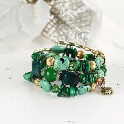 Green boho charm bracelet close-up with mixed green stones, gold beads, and dangling charm.