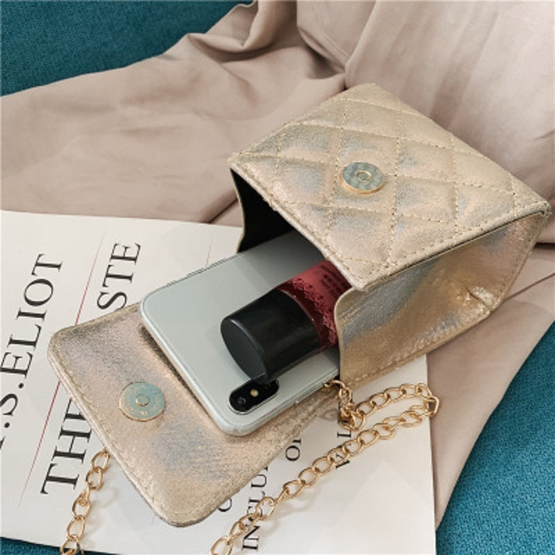 Beige metallic mini quilted crossbody bag with pearl chain and flap front holding phone