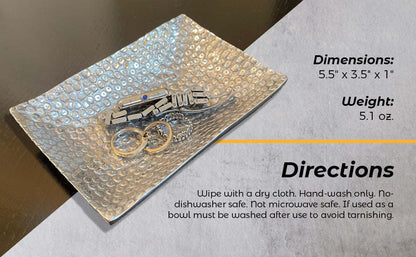Rectangular hammered metal tray holding a pair of jewelry rings and small charms