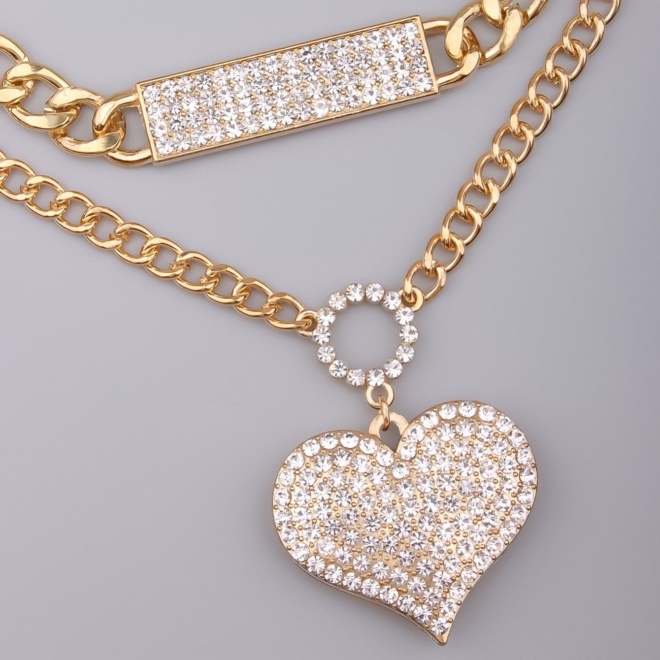 Gold necklace close-up with crystal rectangle bar, round halo charm, heart pendant