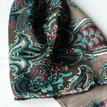 Close-up paisley silk scarf fabric in dark tones with teal and pink swirls