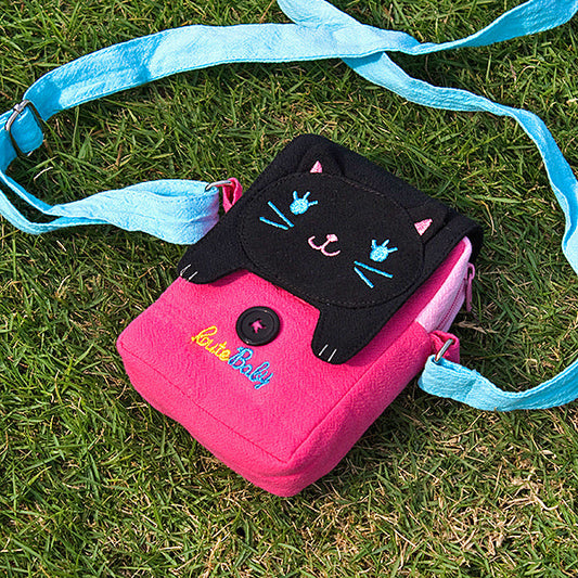 Embroidered cat swingpack bag with pink body, black flap, and light blue shoulder strap.