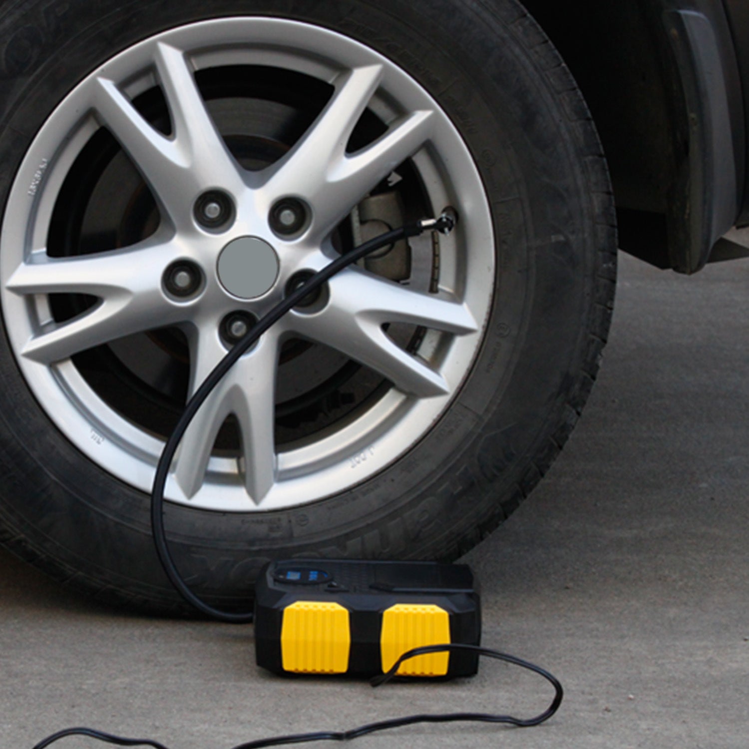 Yellow-and-black tire inflator pump connected to a car wheel valve with hose